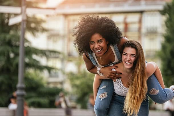 Two happy and confident women having fun in park, one of them riding on the other one