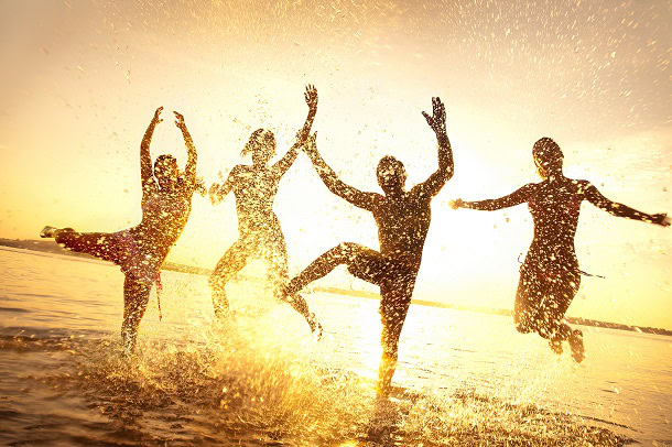 Friends having fun jumping around in the water on the beach at sunset.