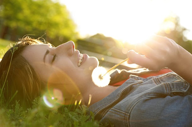 A relaxed woman lying in the grass with a dandelion in her hand.
