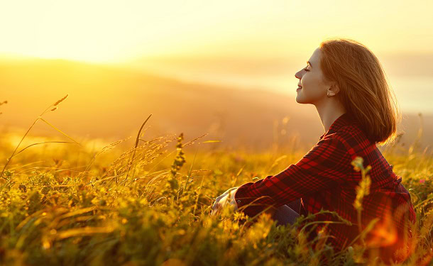 A woman sitting in a field enjoying the sunshine.