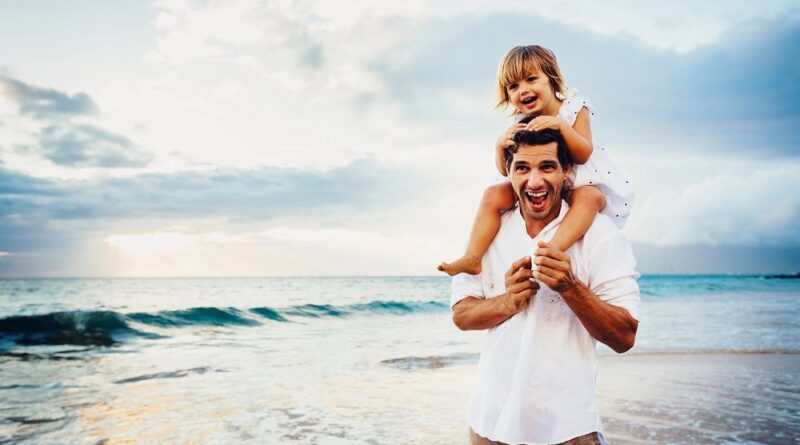A happy dad with a his daughter on his shoulders at the beach.