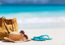 A beach with blue water and a bag, hat, sunglasses and a pair of flip flops.