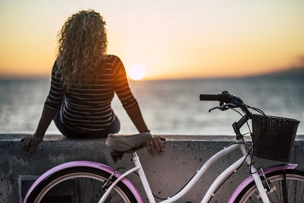 A woman sitting down to enjoy the summer sunset by the ocean.