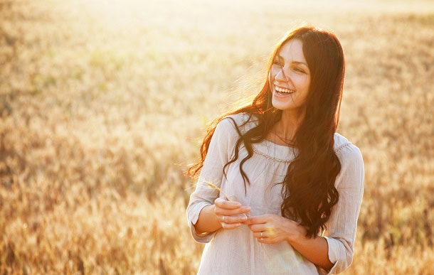 A happy woman standing in the sunshine in a field.