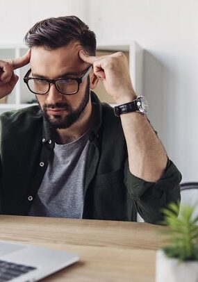 A man sitting by his laptop, thinking and looking frustrated.