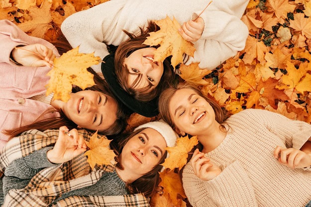 Smiling women lying on the ground in fall leaves.