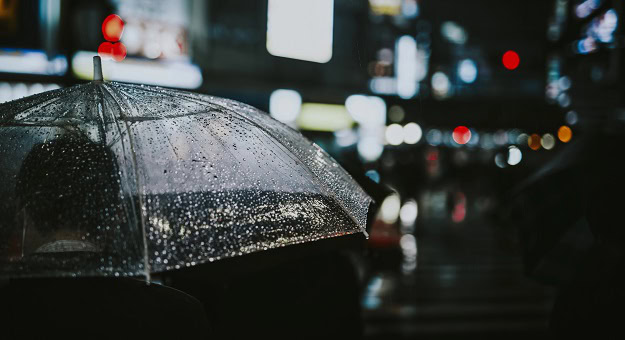 Man with an umbrella in the rain at night.