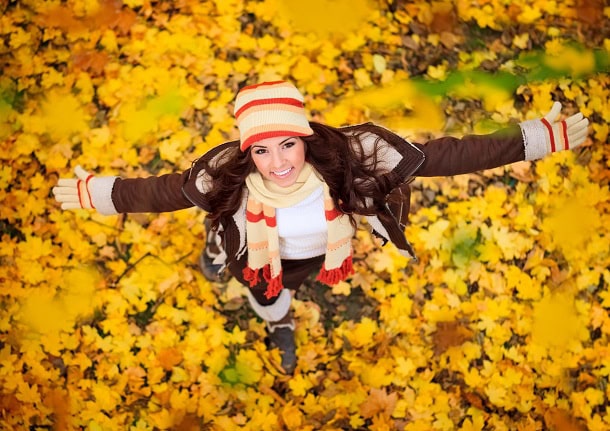 A woman standing in fall leaves with a smile.