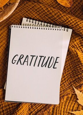 A notebook with the word gratitude written on it and fall leaves around the notebook.