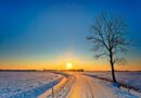 A small road with a beautiful sunrise over a snow covered and open landscape. 