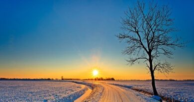 A small road with a beautiful sunrise over a snow covered and open landscape. 