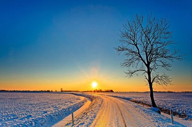A small road with a beautiful sunrise over a snow covered and open landscape.
