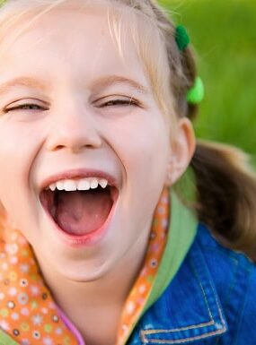 A laughing little girl standing on field of grass.