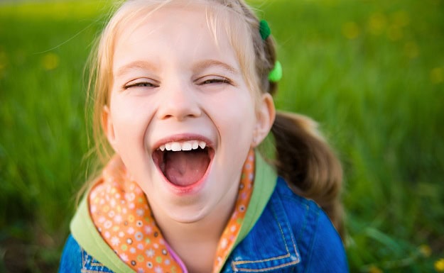 A laughing little girl standing on field of grass.