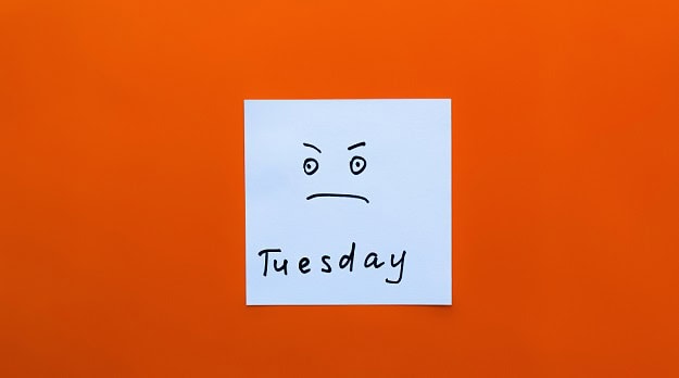 A somewhat irritated or angry smiley on a post-it note with the word Tuesday written below it.