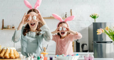 A happy mom and daughter in the kitchen holding up Easter eggs in front of their eyes.