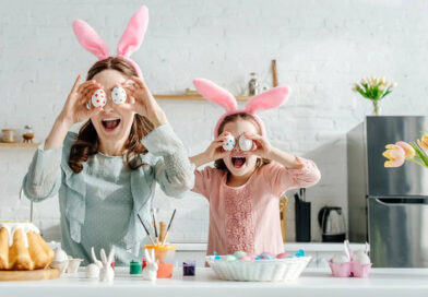 A happy mom and daughter in the kitchen holding up Easter eggs in front of their eyes.