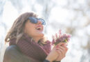 A happy woman outside in the spring sun with a few flowers in her hands.
