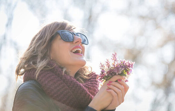 A happy woman outside in the spring sun with a few flowers in her hands.