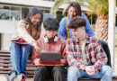 Students looking at a laptop while sitting on a bench outside school.