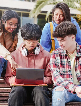 Students looking at a laptop while sitting on a bench outside school.