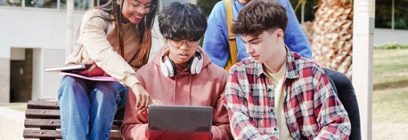 Students looking at a laptop while sitting on a bench outside school.