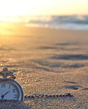 An old pocket watch half buried in the sands of the a beach.