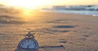 An old pocket watch half buried in the sands of the a beach.