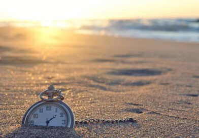 An old pocket watch half buried in the sands of the a beach.