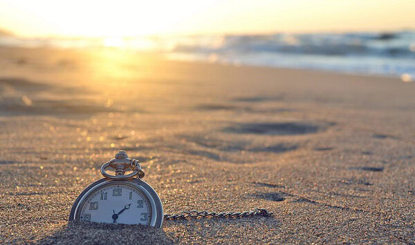 An old pocket watch half buried in the sands of the a beach.