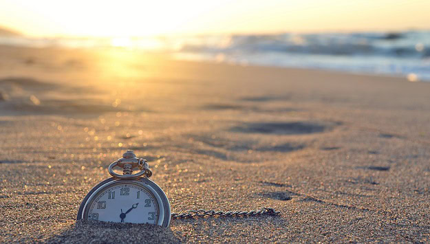 An old pocket watch half buried in the sands of the a beach.