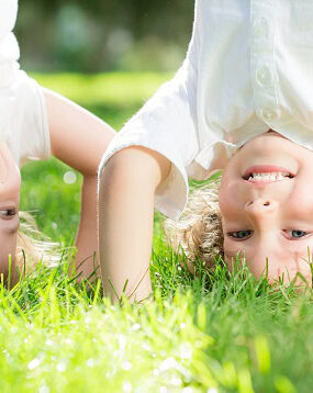 Two kids standing on their hands in the grass and laughing.