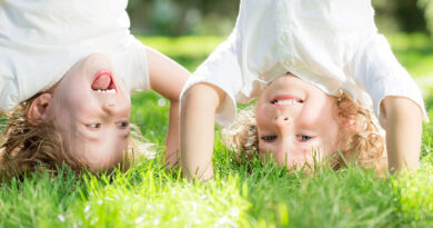 Two kids standing on their hands in the grass and laughing.
