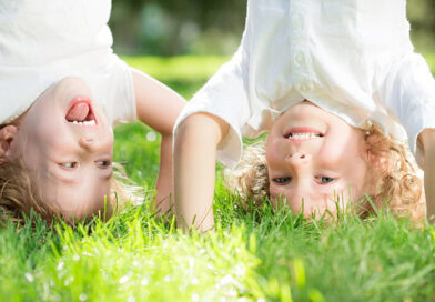Two kids standing on their hands in the grass and laughing.