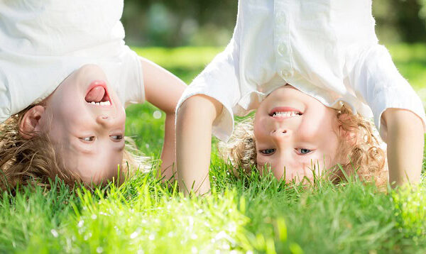 Two kids standing on their hands in the grass and laughing.