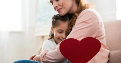 A daughter with a paper heart in her hand in the arms of her loving mother.