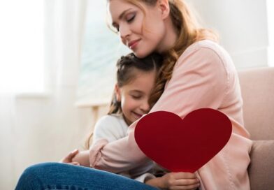 A daughter with a paper heart in her hand in the arms of her loving mother.