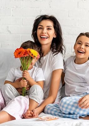 A happy mother with her two smiling children in bed and a bouquet of flowers.
