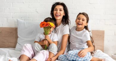 A happy mother with her two smiling children in bed and a bouquet of flowers.