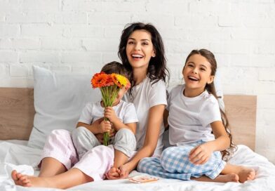 A happy mother with her two smiling children in bed and a bouquet of flowers.