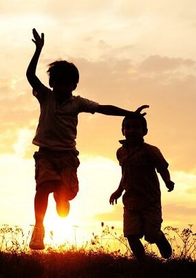Happy kids running in the grass at sunset.