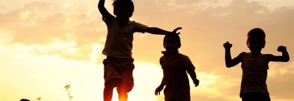 Happy kids running in the grass at sunset.