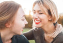 Two women laughing outdoors in the sun.
