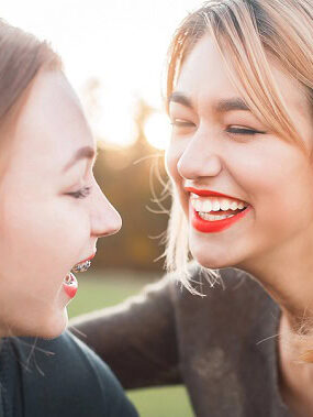 Two women laughing outdoors in the sun.