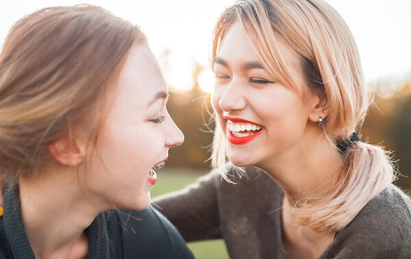 Two women laughing outdoors in the sun.